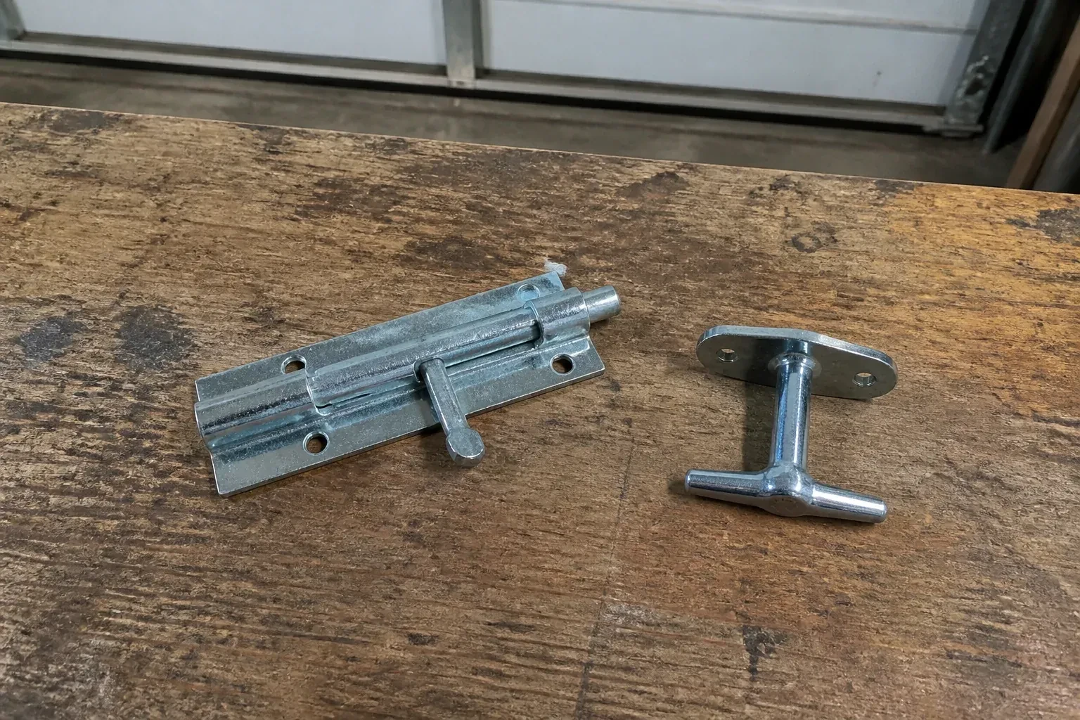 Detached slide bolt and T-handle on a wooden garage workbench. — Garage Door Manual Lock Repair, Halton Hills