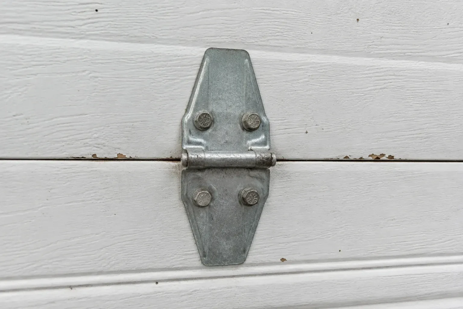 Metal center hinge across a seam in a white sectional garage door. — Garage Door Hinge Replacement, Halton Hills